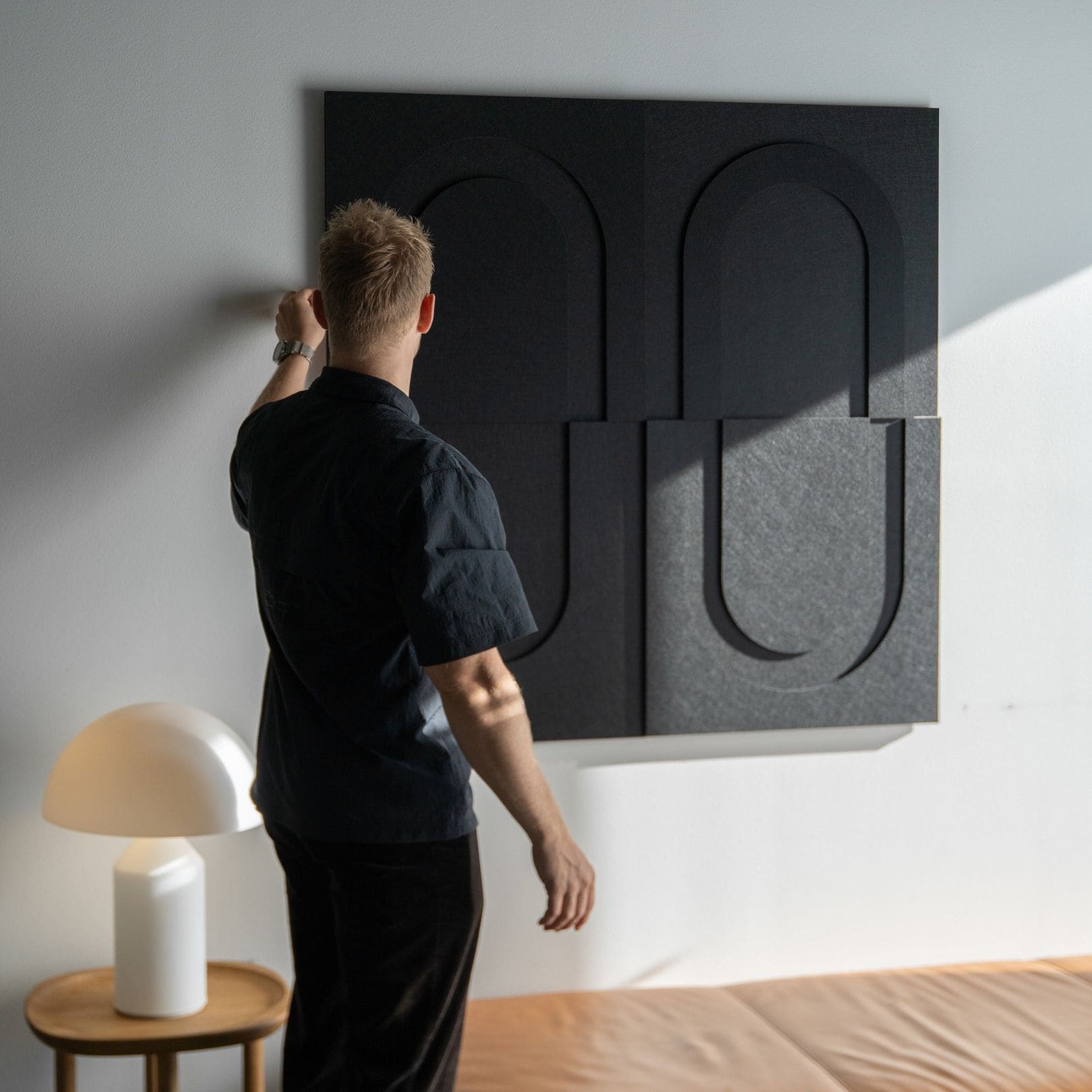 Man installing black geometric soundproof wall art from Arturel, designed for acoustic enhancement in modern interiors.